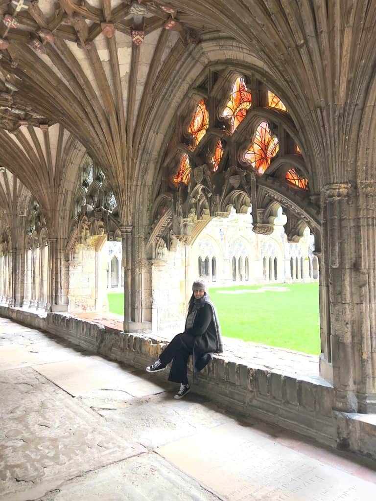 Bejal sitting in Canterbury cathedral Cloisters with stained glass windows